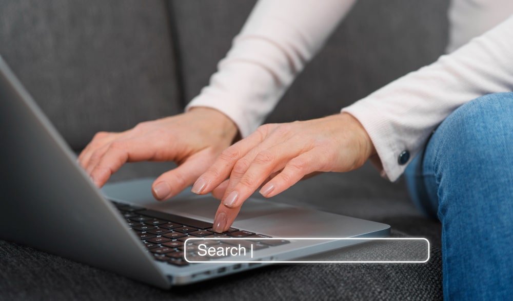 Hånd, der skriver på et laptop tastatur med en søgefelt synlig på skærmen.